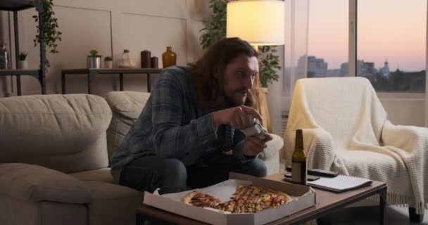 Man enjoying pizza and beer playing video game at home - Filmmaterial, Video
