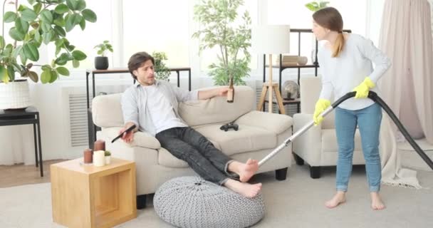Woman vacuuming carpet quarrels husband drinking beer and watching tv - Filmmaterial, Video