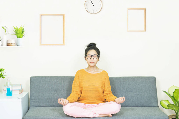 pessoas e lazer conceito -Jovem mulher asiática meditar no sofá descansando nos fins de semana em casa sob quarentena
 - Foto, Imagem