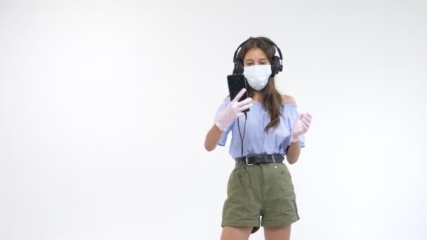 white background. girl in gloves and a medical mask in headphones makes selfie - Metraje, vídeo