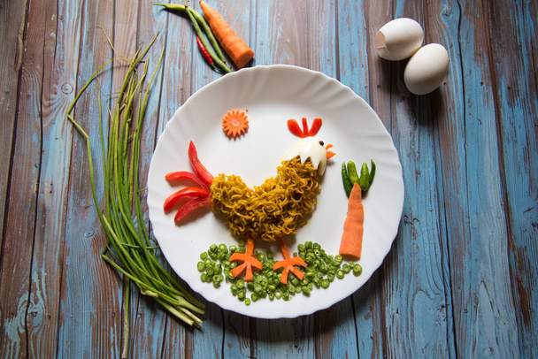 Élelmiszer-művészet a háttérben tészta, zöldség, tojás formájában kakas egy tányéron, szelektív fókusz. - Fotó, kép