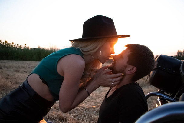 Bikers man and woman stopped at the side of the road to rest and kiss passionately. Photos of loving motorcyclists at sunset. The concept of freedom, brutality and passion - Zdjęcie, obraz