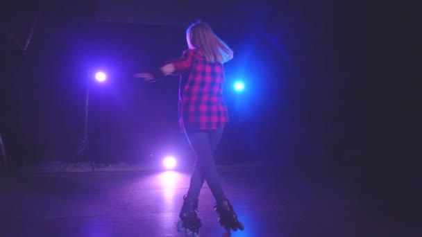 Close-up panoramic view of beautiful young roller skater woman, technically spinning on front wheels in one place under light of spotlights on dark stage in slow motion. Performance by active girl. - Footage, Video
