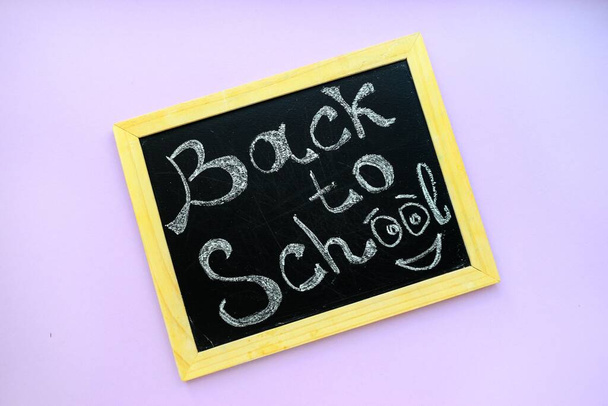 Inscription back to school on a black chalkboard with a wooden frame on a purple background. - Фото, изображение