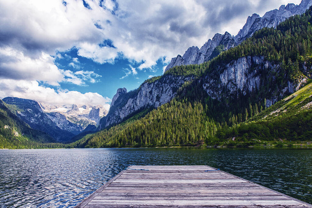 Piękny krajobraz jeziora Gosausee z górami Dachstein, łódź, las, chmury i odbicia w wodzie w Alpach Austriackich. region Salzkammergut. - Zdjęcie, obraz