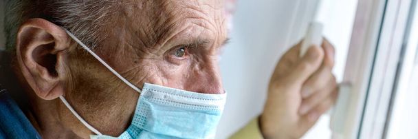 wrinkled man in blue face mask holds window handle closeup - Fotó, kép