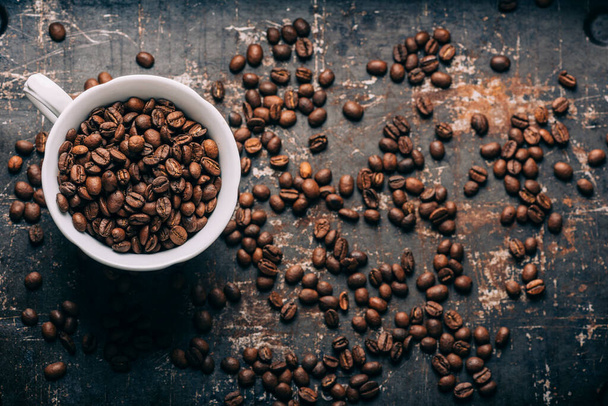 コーヒー豆の質感と黒素朴な背景にコーヒーカップのトップビュー。ヴィンテージのダークテーブルの上のホットドリンク。レストランカフェショップ創造的なメニュー. - 写真・画像