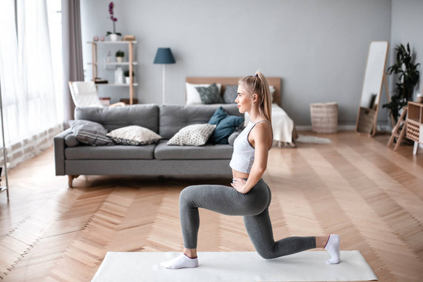Fit woman in sportswear is doing squat exercises at home. Physical exercise indoors. - Fotó, kép