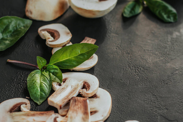 Champignon slices and basil leaves on a black background copy space. - Foto, afbeelding
