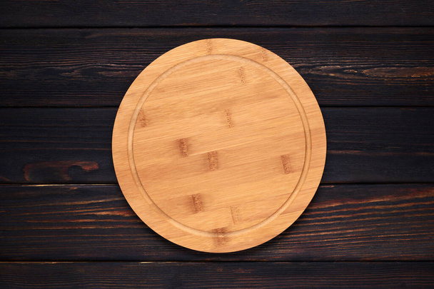 Multifunctional circular wooden cutting board for pizza, bread or steak serve. Top view on wooden kitchen table. Copy space  - Foto, afbeelding
