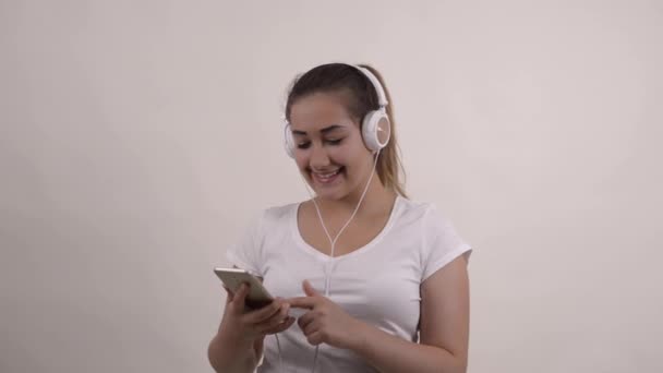 Beyaz tişörtlü güzel kız, kulaklıkla müzik dinlemek için telefonu kullan. - Video, Çekim