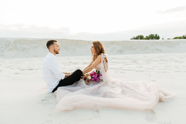 Love Story van een mooi koppel in een roze bruiloft luxe jurk met een boeket in de Sahara woestijn, zand, duinen - Foto, afbeelding