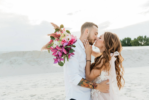 Love Story di una bella coppia in un abito da sposa rosa di lusso con un bouquet nel deserto del Sahara, sabbia, dune - Foto, immagini