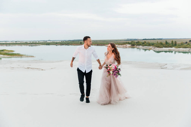 Love Story of a beautiful couple in a pink wedding luxury dress with a bouquet in the Sahara desert, sand, dunes - Fotó, kép