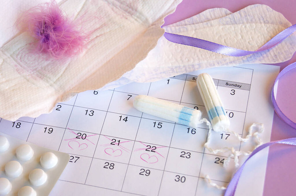 Menstruationskissen und Tampons auf Menstruationskalender mit fliederfarbenem Hintergrund. - Foto, Bild
