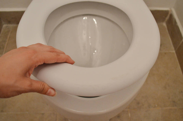 Toalete branco moderno em um banheiro. Mão feminina pega a borda branca do vaso sanitário
 - Foto, Imagem