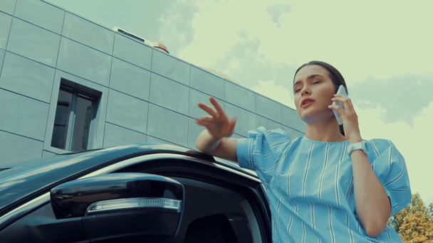 jovem mulher apoiando-se no carro e gesticulando enquanto fala no smartphone
 - Filmagem, Vídeo