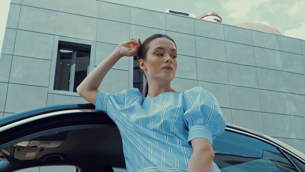 όμορφη, σαγηνευτική γυναίκα αγγίζει τα μαλλιά, ενώ θέτουν κοντά στο αυτοκίνητο - Πλάνα, βίντεο