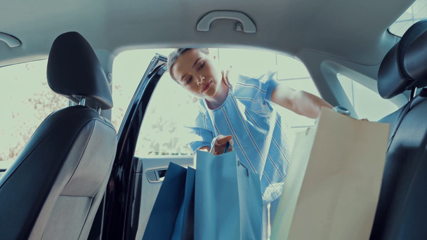 atrakcyjna kobieta biorąc torby na zakupy z tylnego siedzenia samochodu - Materiał filmowy, wideo