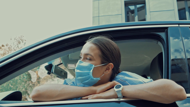 kobieta w masce medycznej siedzi na fotelu kierowcy i patrzy przez otwarte okno - Materiał filmowy, wideo