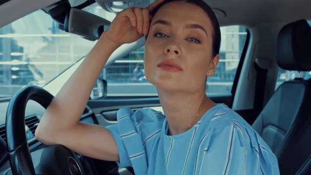 atrakcyjna, flirciarska kobieta patrząca w kamerę siedząc na fotelu kierowcy w samochodzie - Materiał filmowy, wideo