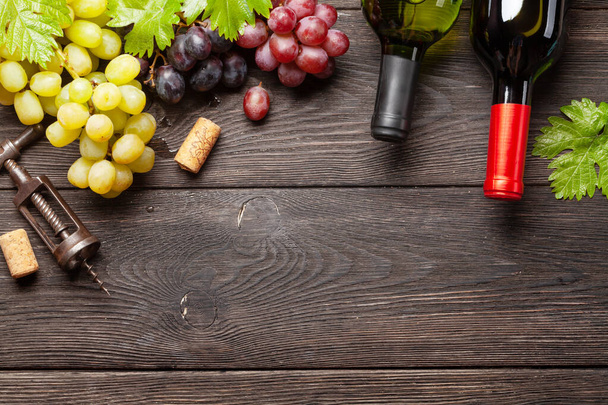 Various grapes, wine bottles and corkscrew on wooden table. Top view with copy space. Flat lay - Photo, Image