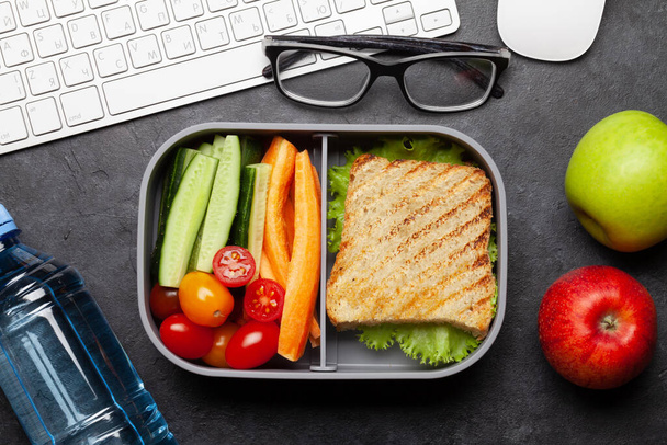 Sano cestino per il pranzo con sandwich e verdure sul tavolo dell'ufficio. Vista dall'alto. Posa piatta - Foto, immagini