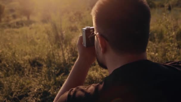 Close-up of a young man taking pictures in nature with a retro camera. Video from behind. Charismatic young man sets the camera - Footage, Video