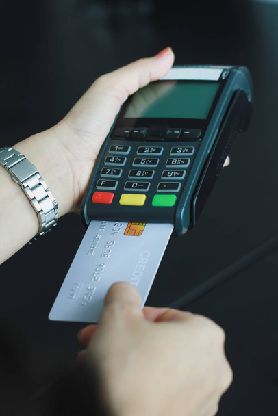 Een vrouw die met de hand credit card swipe machine voor de verkoop van producten in de winkel. Begrip uitgaven via kredietkaart. - Foto, afbeelding