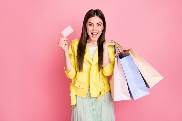 Photo of pretty lady choosing clothes hold many shopping packs plastic bonus card buying new collection wear trend yellow leather jacket skirt isolated pastel pink color background - 写真・画像