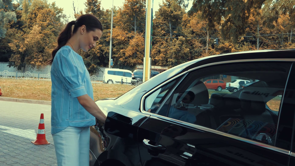 Lächelnde Frau tankt Auto und holt Tankpistole aus Auto an Tankstelle - Filmmaterial, Video