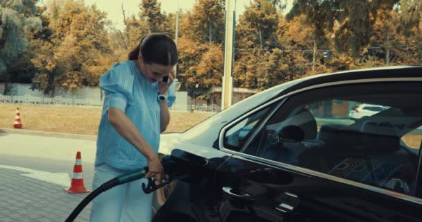 happy woman talking on smartphone while refueling car on gas station - Filmmaterial, Video