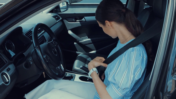 молодая женщина пристегивает ремни безопасности, сидя на водительском сидении в машине  - Кадры, видео