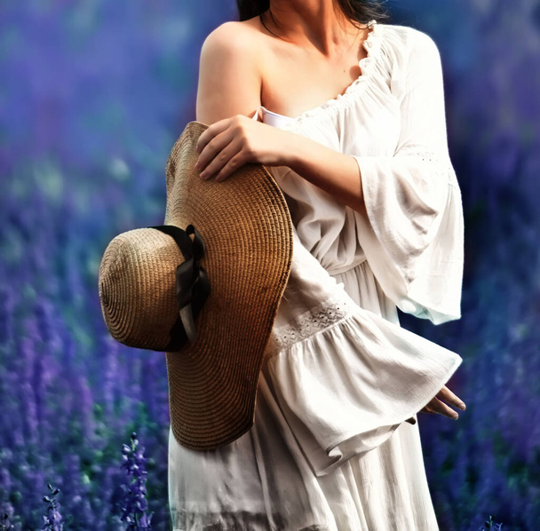 A girl in a white dress and a straw hat in a lush lilac field. the atmosphere of a summer holiday in the countryside. A girl without a face.Selective soft focus. - Φωτογραφία, εικόνα