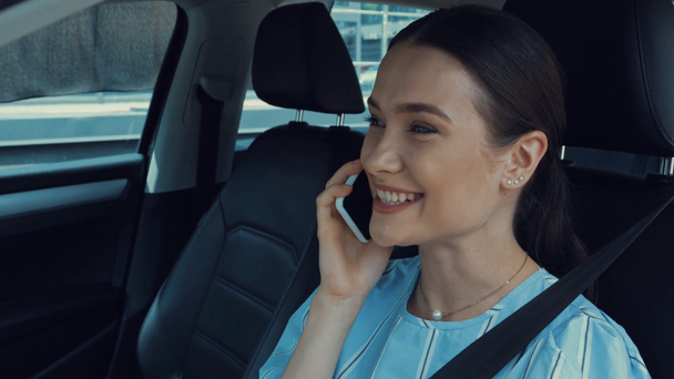 Mutlu, çekici bir kadın arabada oturuyor ve akıllı telefondan konuşuyor. - Video, Çekim
