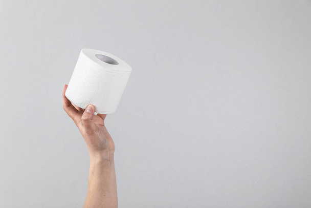 Female hand holds a soft roll of toilet paper on a gray background with copy space. Composition for advertising, article or banner - Photo, Image