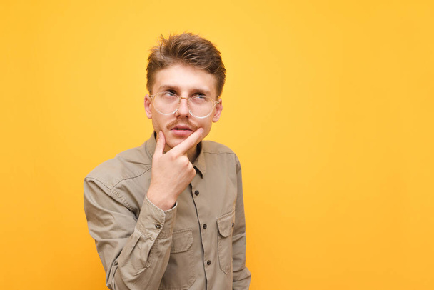 Nahaufnahme Porträt eines nachdenklichen jungen Mannes in Hemd und Brille vor gelbem Hintergrund, der wegschaut und denkt. Nerd mit Schnurrbart und Brille auf gelbem Hintergrund. - Foto, Bild