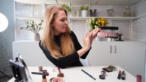 Beauty blogger woman filming daily makeup routine tutorial near camera. Influencer girl live streaming cosmetics product review. Vlogger female recommends eye shadow palette, teaches in masterclass. - Materiaali, video
