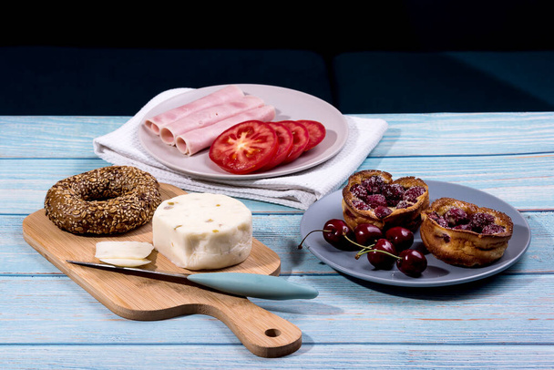 Το πρωινό σερβίρεται σε μπλε ξύλινο τραπέζι με χυμό, ζαμπόν, τυρί πεκορίνο, ντομάτα, κουλούρι καλαμποκιού και γλυκιά κερασόπιτα. Continental νόστιμο υγιεινό πρωινό τραπέζι - Φωτογραφία, εικόνα