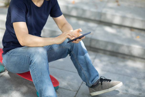 asiatico donna sedersi su skateboard utilizzando smartphone in moderno città - Foto, immagini