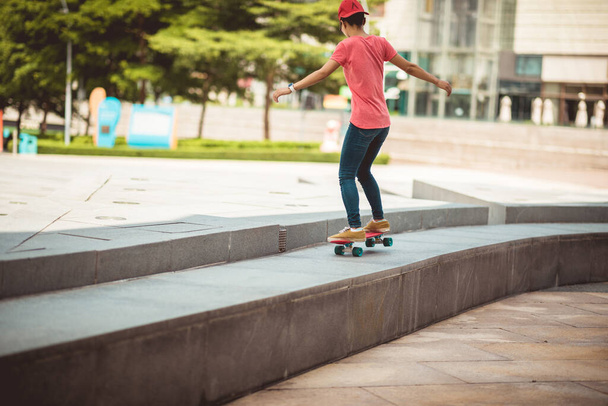 Asian woman skateboarder skateboarding in modern city - Fotó, kép