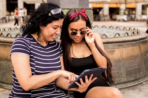 Selektiver Fokus junger Frauen, die über einen Platz in der Stadt laufen und dabei ihre elektronischen Geräte benutzen - Foto, Bild