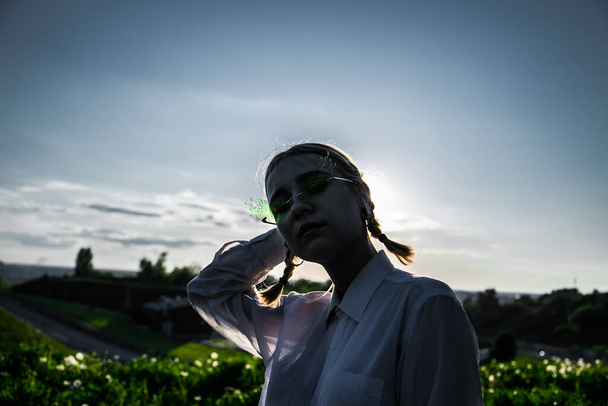 A girl with pigtales in green sunglasses outdoors at sunset - Foto, immagini