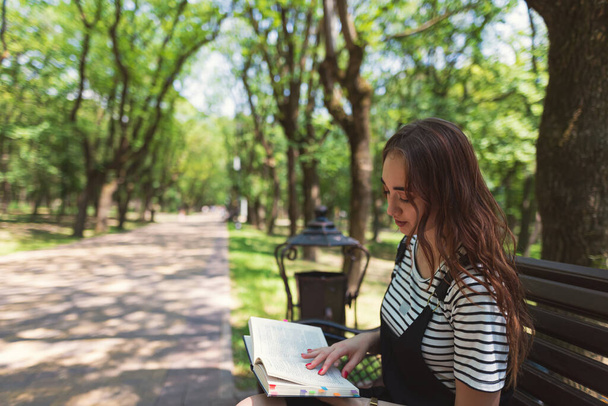 Bájos vörös hajú tini lány a parkban könyvet olvas egy padon, és felkészülés a vizsgára - Fotó, kép