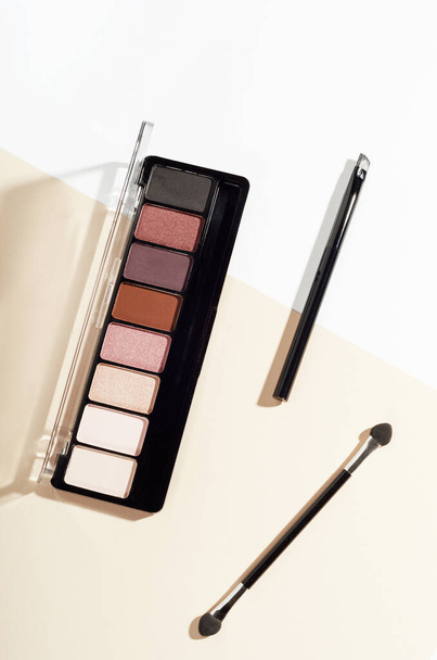 Eye shadow palette and brush top view image. Cosmetic facial care product isolated on beige background. Makeup accessories, feminine fashion attribute. Eyeshadow powder and eye liner kit. - 写真・画像