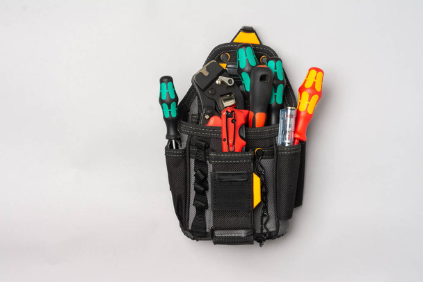 A black electrician's or Builder's bag with tools on a gray table. Bag with construction tools: screwdrivers, knife, crimping on a gray background. Top view with space for text - Fotó, kép