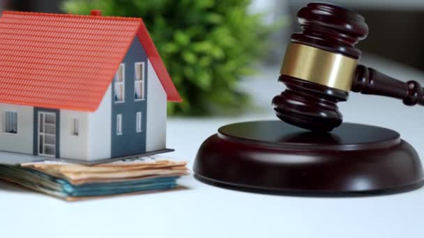Miniature plastic house staying on stack of money near the wooden judge gavel, property auction concept. Financial transactions, investment and expenses during buying or selling house process - Footage, Video