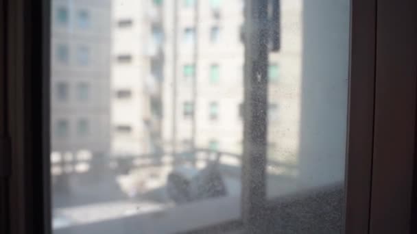 Zbliżenie brudnego szkła okiennego z zamazanym tłem dzielnicy mieszkalnej, kurzem i zaschniętymi kroplami wody na szklanym sufrażu, starym opuszczonym mieszkaniu z brudnym oknem. Warunki antyhigieniczne i niehigieniczne - Materiał filmowy, wideo