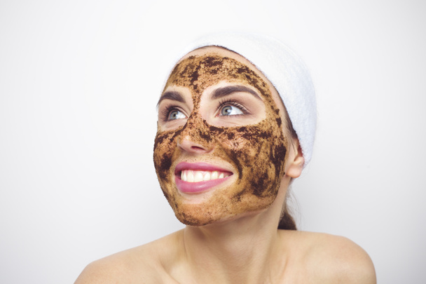 Coffee grounds on the face of a smiling young woman. Scrubbing. Facial cleansing in a beauty salon. - Photo, Image