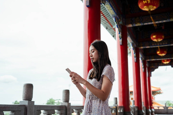 Cute młoda azjatycka kobieta za pomocą smartfona podczas podróży w chińskim wielkim pałacu lub świątyni. - Zdjęcie, obraz